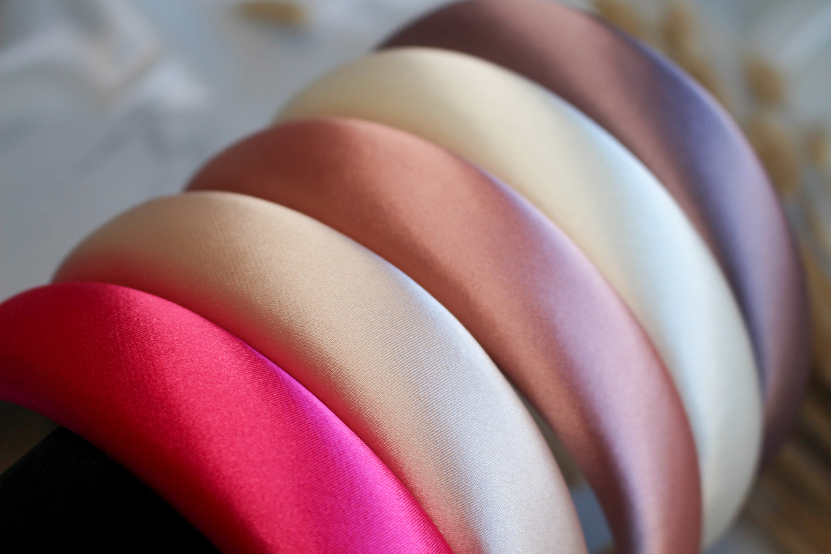 A collection of padded satin headbands in various colors, including beige, white, brown, pink, and red.